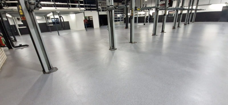 Nieuw aangebrachte grijze vloercoating in een ruime garage met meerdere metalen steunpilaren.
